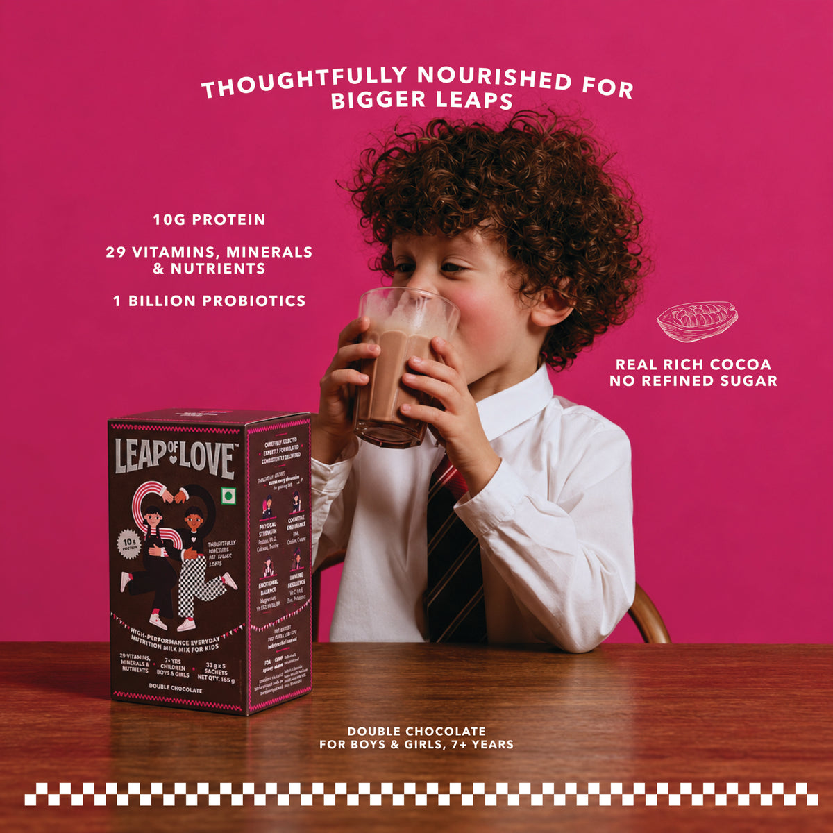 Boy in a white school shirt drinking Leap of Love Double Chocolate milk, with the 165 g trial pack box on a wooden table
